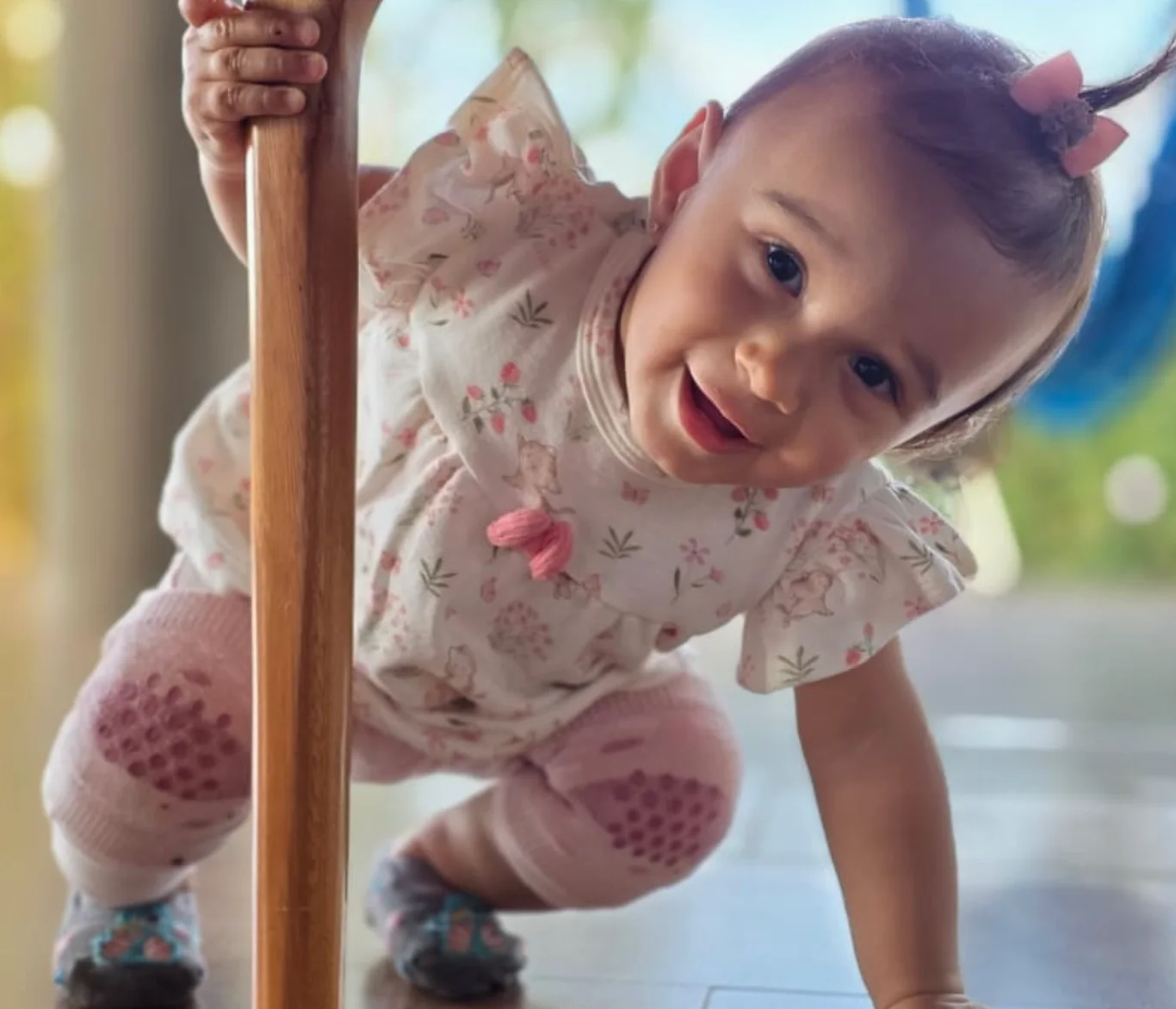 Antonella agachada segurando o pé de madeira da mesa, rindo para a câmera