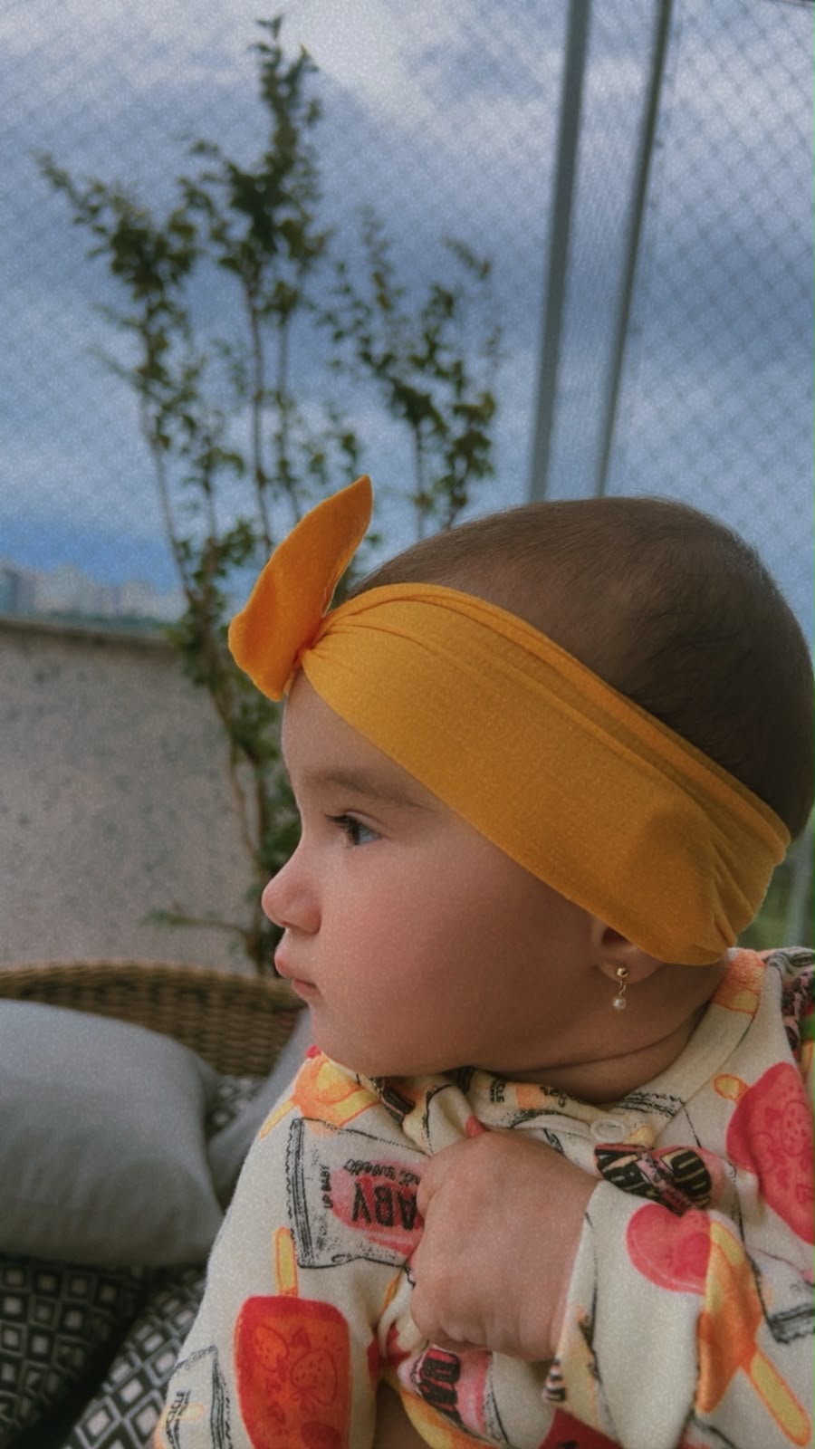 Antonella de perfil, com laço amarelo na cabeça, olhando o horizonte